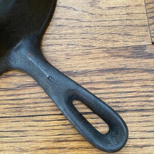 May include: A black cast iron skillet with a single handle. The handle has a small hole in it. The skillet is on a wooden surface.