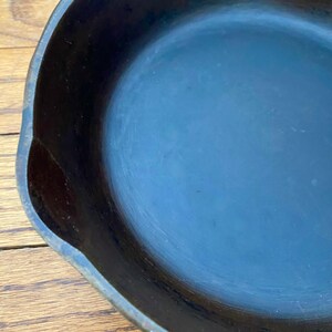 May include: A black cast iron skillet with a smooth, dark blue interior. The skillet is empty and appears to be well-seasoned.