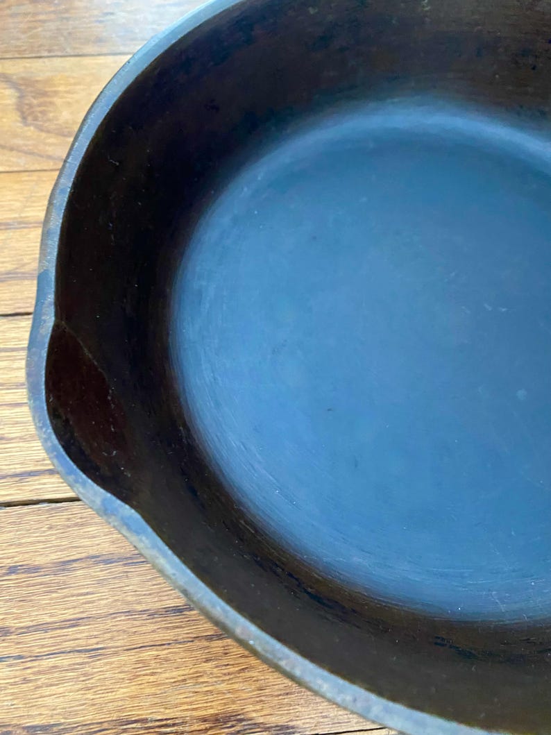 May include: A black cast iron skillet with a smooth, dark blue interior. The skillet is empty and appears to be well-seasoned.
