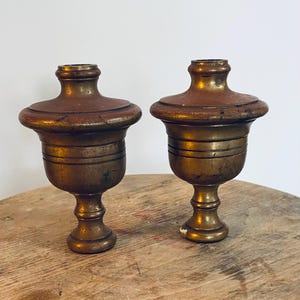 May include: Two antique brass finials with a brown patina. The finials have a round top and a fluted base.