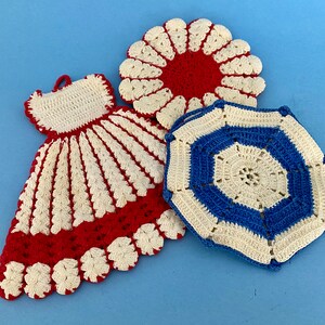 May include: Three handmade crochet items: a red and white dress-shaped hot pad, a red and white flower-shaped hot pad, and a blue and white geometric hot pad. The items are displayed on a light blue surface.