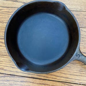 May include: A black cast iron skillet with a 5 stamped on the handle.