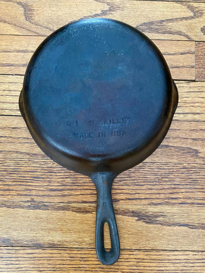 May include: A black cast iron skillet with a handle. The bottom of the skillet is marked with the text "8" "1" "SKILLET" "MADE IN USA".