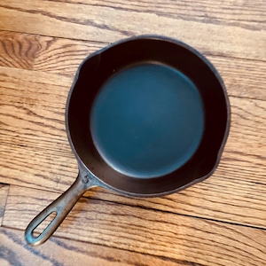 May include: A black cast iron skillet with a handle. The skillet is empty and has a smooth surface. The number "5" is visible on the handle.