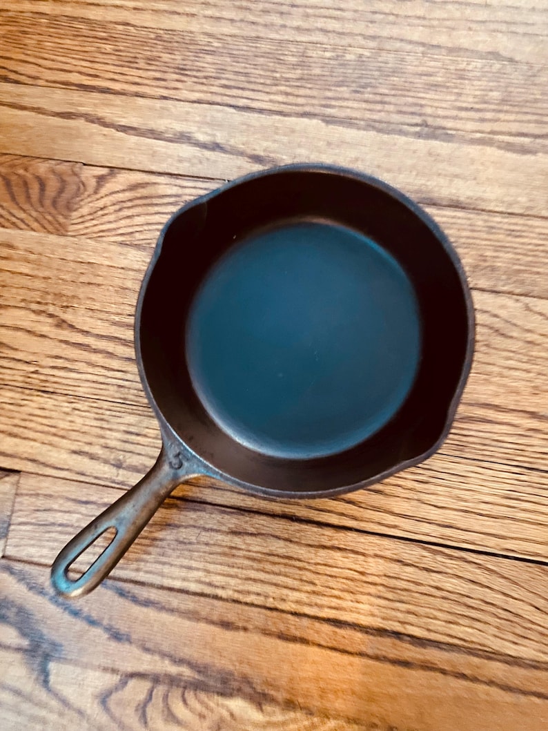 May include: A black cast iron skillet with a handle. The skillet is empty and has a smooth surface. The number "5" is visible on the handle.