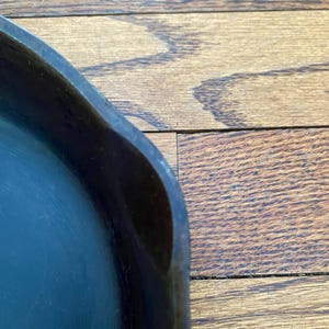 May include: Close-up of the edge of a black cast iron skillet. The skillet is on a wooden surface.