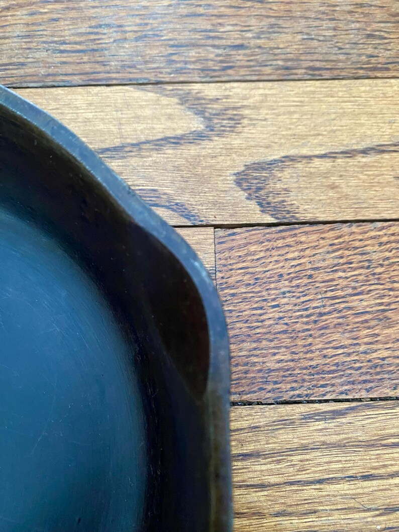 May include: Close-up of the edge of a black cast iron skillet. The skillet is on a wooden surface.