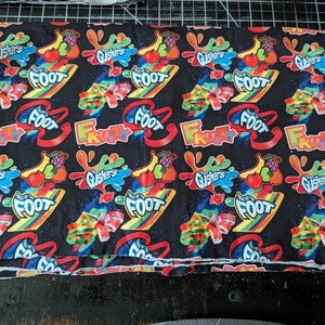 May include: Black fabric with a repeating pattern of colorful Gushers and Fruit by the Foot candy graphics. The design includes fruit illustrations, rainbow stripes, and the words "Gushers" and "Fruity Foot".