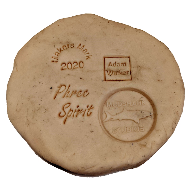 K&ouml;nnte beinhalten: Eine beige Tonplatte mit mehreren Stempeln. Die Stempel beinhalten "Makers Mark 2020", "Adam Walker", "Phree Spirit" und "Mudshark Studios" mit einer Haifischsilhouette.