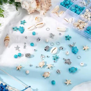 May include: A collection of jewelry making supplies including turquoise and white beads, silver-toned metal charms shaped like sea turtles, dolphins, and starfish, and small white seashells scattered on a light blue and white surface.