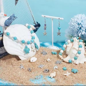 May include: A collection of jewelry featuring two beaded bracelets and a pair of drop earrings with turquoise and white beads. The set includes silver-toned charms shaped like sea turtles and starfish, displayed alongside loose beads and charms.