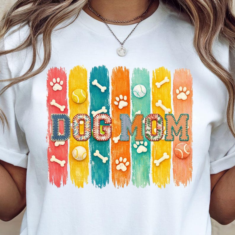 Colorful dog mom graphic with vertical painted stripes, paw prints, bones, and tennis balls in a playful patchwork style design for shirts and sublimation.