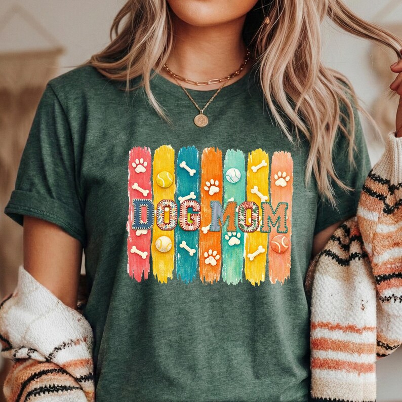 Colorful dog mom graphic with vertical painted stripes, paw prints, bones, and tennis balls in a playful patchwork style design for shirts and sublimation.