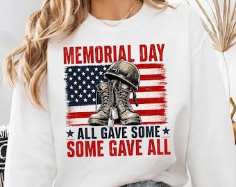 May include: White sweatshirt with a graphic design for Memorial Day. The design features a US flag, combat boots, a helmet, and dog tags. Text reads "MEMORIAL DAY" and "ALL GAVE SOME, SOME GAVE ALL."