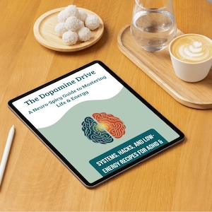 Peut inclure: Une tablette numérique affiche la couverture du livre "The Dopamine Drive: A Neuro-Spicy Guide to Mastering Life & Energy". La couverture présente un cerveau divisé. Un stylet, du café et des collations sont également visibles.