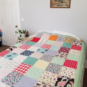 May include: A patchwork quilt with a variety of colors and patterns, including red, blue, green, and white. The quilt is made up of squares of different fabrics, and it is laid out on a bed.