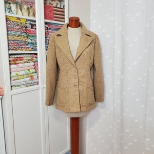 May include: A brown tweed blazer with a single button closure and two patch pockets. The blazer is on a wooden mannequin.