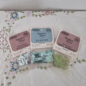 Peut inclure: Trois petits sachets en plastique transparent contenant des sequins et paillettes Walbead Fashion Trims. Le sachet de gauche contient des sequins cup de 8 mm, celui du centre des sequins plats de 6 mm et celui de droite des paillettes en croissant.