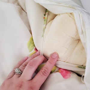 Puede incluir: Una funda n&oacute;rdica blanca con un estampado floral en tonos verdes, rosas y amarillos. La funda n&oacute;rdica est&aacute; doblada hacia atr&aacute;s para revelar un edred&oacute;n de plum&oacute;n blanco.