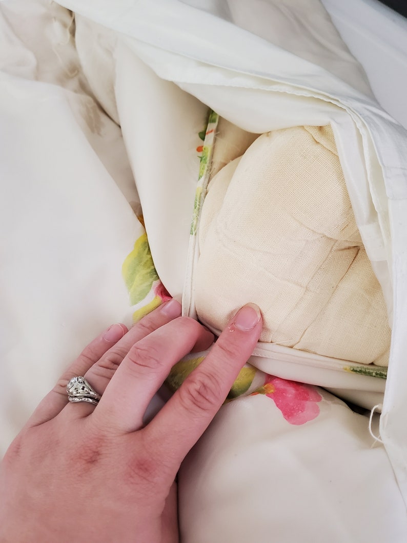 Puede incluir: Una funda n&oacute;rdica blanca con un estampado floral en tonos verdes, rosas y amarillos. La funda n&oacute;rdica est&aacute; doblada hacia atr&aacute;s para revelar un edred&oacute;n de plum&oacute;n blanco.