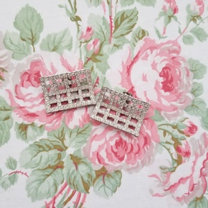 May include: A pair of silver tone clip-on earrings with a square grid design set with clear rhinestones.