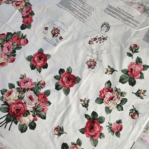 May include: A white fabric panel featuring printed sewing patterns for a sweatshirt and tote bag, accompanied by detailed instructions and illustrations of a person wearing the garment. The fabric is decorated with various red and pink rose bouquets.