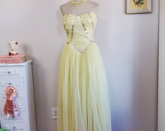 May include: A strapless yellow tulle gown with silver sequins and beading. The gown has a fitted bodice and a full skirt. The gown is on a mannequin and is displayed against a white wall.