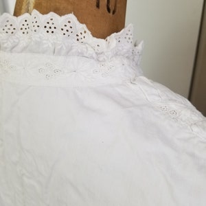 May include: White cotton blouse with a lace collar. The collar has a scalloped edge and eyelet embroidery.