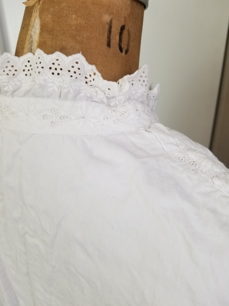 May include: White cotton blouse with a lace collar. The collar has a scalloped edge and eyelet embroidery.