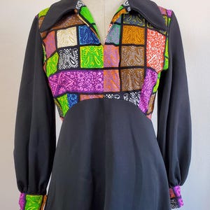 Puede incluir: Un vestido negro de manga larga con un estampado de patchwork colorido en el corpiño y los puños. El estampado presenta motivos paisley y formas geométricas en tonos de verde, rosa, azul, naranja y marrón.