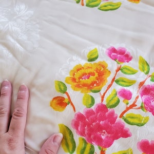 Puede incluir: Tela blanca con un patr&oacute;n floral. Las flores son rosas, amarillas y naranjas con hojas verdes. La tela tiene una superficie texturizada.