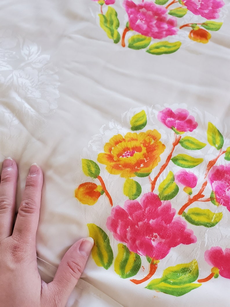 Puede incluir: Tela blanca con un patr&oacute;n floral. Las flores son rosas, amarillas y naranjas con hojas verdes. La tela tiene una superficie texturizada.