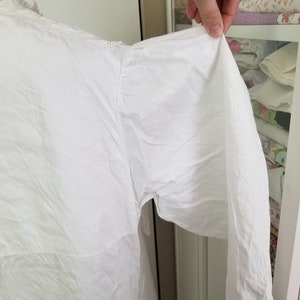 May include: White cotton blouse with a frilled collar and long sleeves. The sleeves are gathered at the shoulder and have a loose, flowing fit.