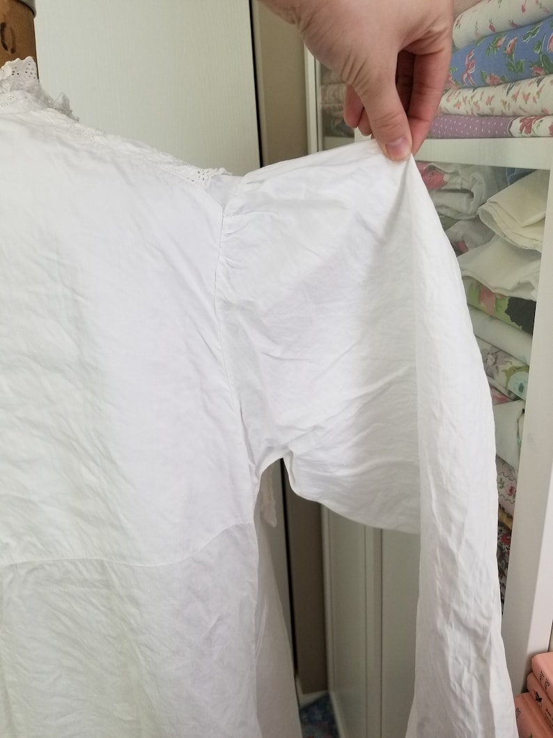 May include: White cotton blouse with a frilled collar and long sleeves. The sleeves are gathered at the shoulder and have a loose, flowing fit.