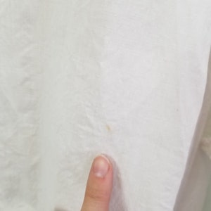 May include: Close-up of a white fabric surface with a small yellow stain.