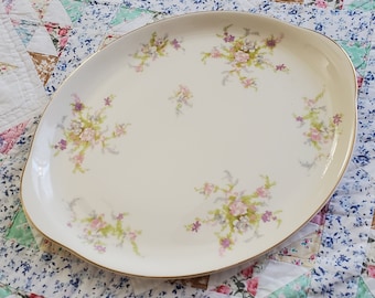 May include: A white oval serving platter with a gold rim and a floral design in shades of pink, purple, and green.
