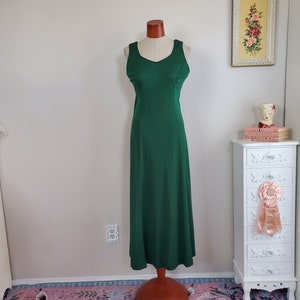 May include: A long, sleeveless, emerald green dress with a V-neckline. The dress is on a wooden dress form and is displayed on a pink floral rug.