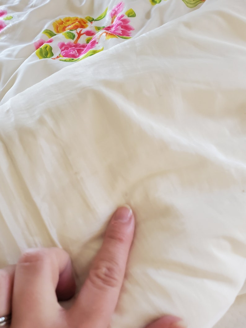 Puede incluir: Primer plano de un edred&oacute;n blanco con un patr&oacute;n floral. El edred&oacute;n est&aacute; hecho de una tela suave y lisa y tiene un brillo sutil.