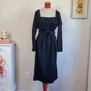 May include: A black midi dress with long sleeves and a square neckline. The dress has a belt at the waist and a slightly flared skirt.