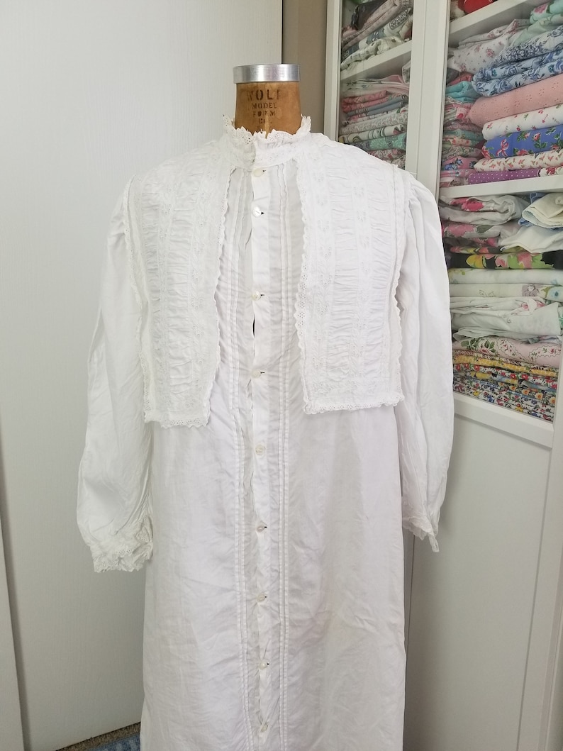 May include: A white cotton nightgown with a lace trim and a button-up front. The nightgown has a high neckline and long sleeves.