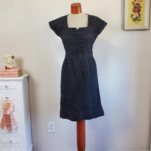 Puede incluir: Un vestido negro sin mangas con escote cuadrado y un patrón geométrico. El vestido es entallado y tiene un dobladillo hasta la rodilla.