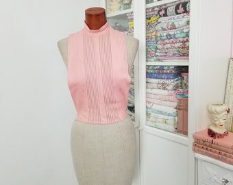 May include: A pink sleeveless blouse with a high neck and vertical pleats. The blouse is displayed on a dress form.