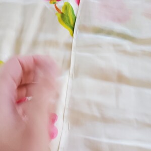 Puede incluir: Primer plano de una tela blanca con una costura que recorre el centro. La tela del lado izquierdo tiene un patr&oacute;n floral con flores rosas y hojas verdes. La tela del lado derecho es blanca lisa.