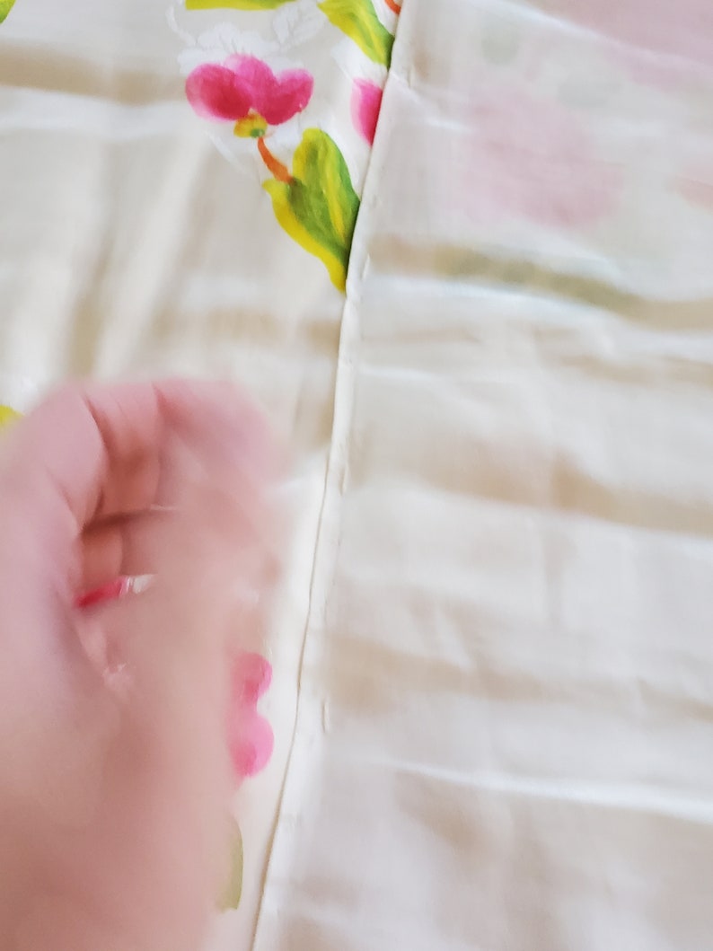 Puede incluir: Primer plano de una tela blanca con una costura que recorre el centro. La tela del lado izquierdo tiene un patr&oacute;n floral con flores rosas y hojas verdes. La tela del lado derecho es blanca lisa.