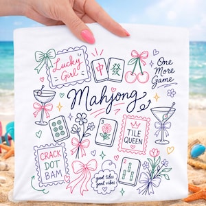 Könnte beinhalten: Ein weißes Stoffquadrat mit farbenfrohen Strichzeichnungen von Mahjong-Steinen, Martinigläsern, Kirschen, Blumen und Schleifen. Der Text umfasst Lucky Girl, One More Game, Mahjong, Tile Queen, Crack Dot Bam und good tiles good vibes.