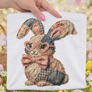 May include: A white square fabric featuring a patchwork bunny design. The bunny wears heart-shaped glasses and a bow tie, with a floral and denim patchwork pattern. The background is a blurred outdoor scene with Easter decorations.