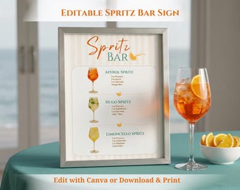 May include: A framed sign with the text "Spritz Bar" and cocktail recipes. The sign features illustrations of Aperol, Hugo, and Limoncello Spritz cocktails. A glass of Aperol Spritz with an orange slice and a bowl of orange slices are on the table.