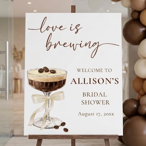 May include: A white rectangular sign featuring the brown text love is brewing, WELCOME TO ALLISON'S BRIDAL SHOWER, and August 17, 20xx. An illustration of a cocktail glass filled with dark liquid, topped with coffee beans, and tied with a cream ribbon.