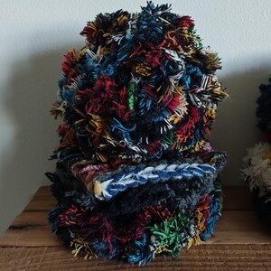 May include: A stack of colorful, textured fabric items. The items are made of various colors of yarn, including red, yellow, blue, and green. The items are stacked on top of each other, creating a visually interesting display.