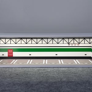 May include: A miniature garage diorama with a white and gray exterior. The interior features green and white striped walls, a gray floor with white lines, and a black truss ceiling. Includes a red sign with Japanese text.